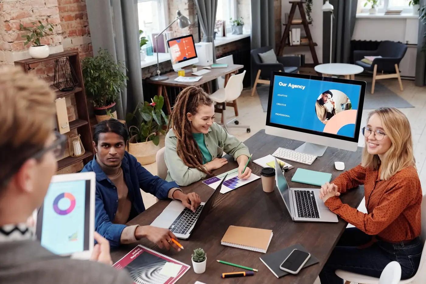 Agency team around a studio table with a brand layout open on the monitor behind them