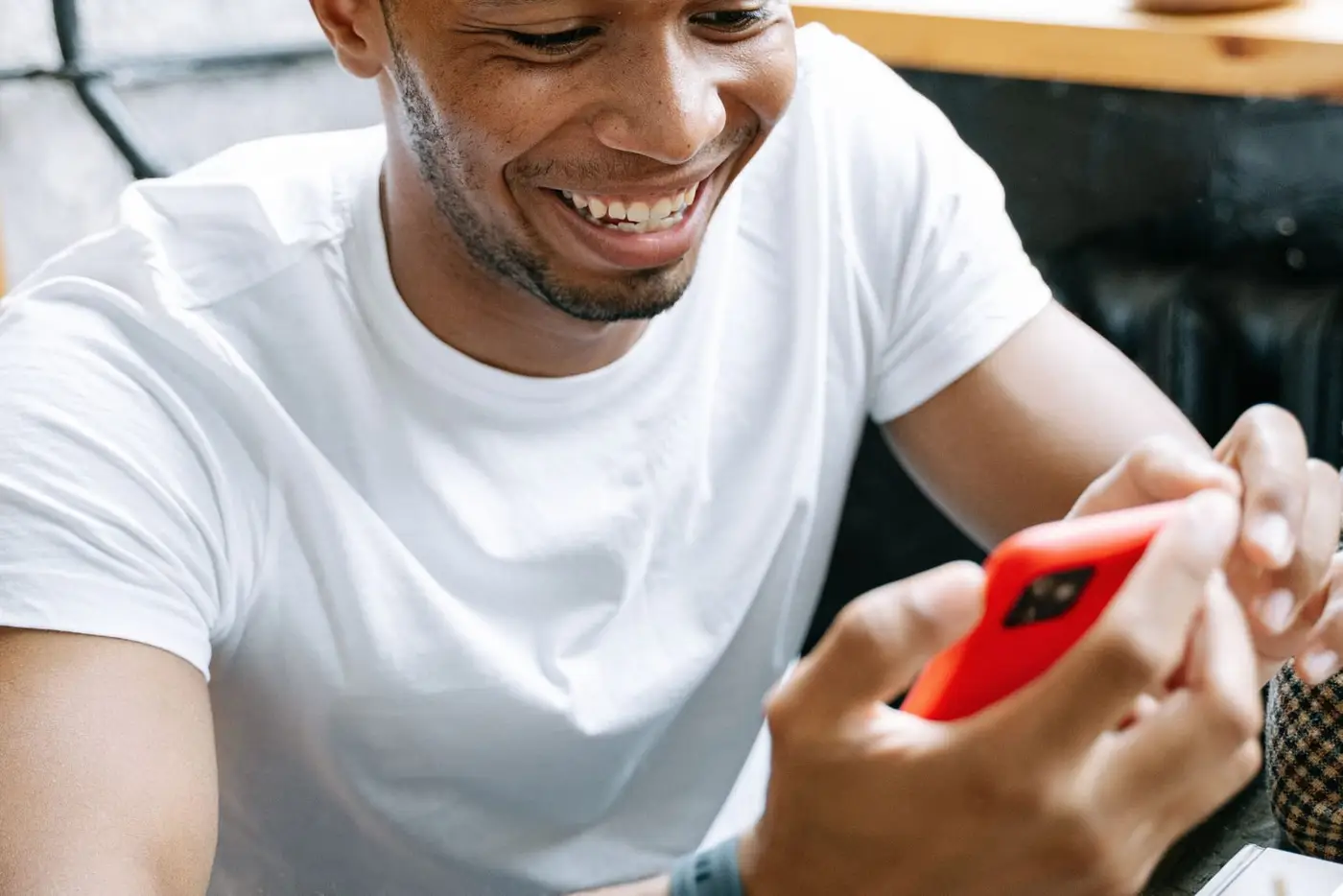 Man laughing at something on his phone across a café table