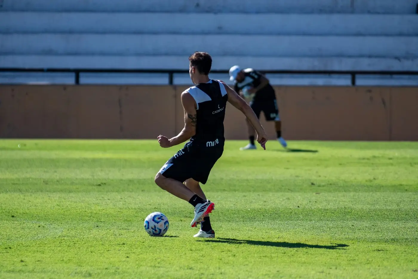 Footballer running onto the ball on a pitch in front of empty stands